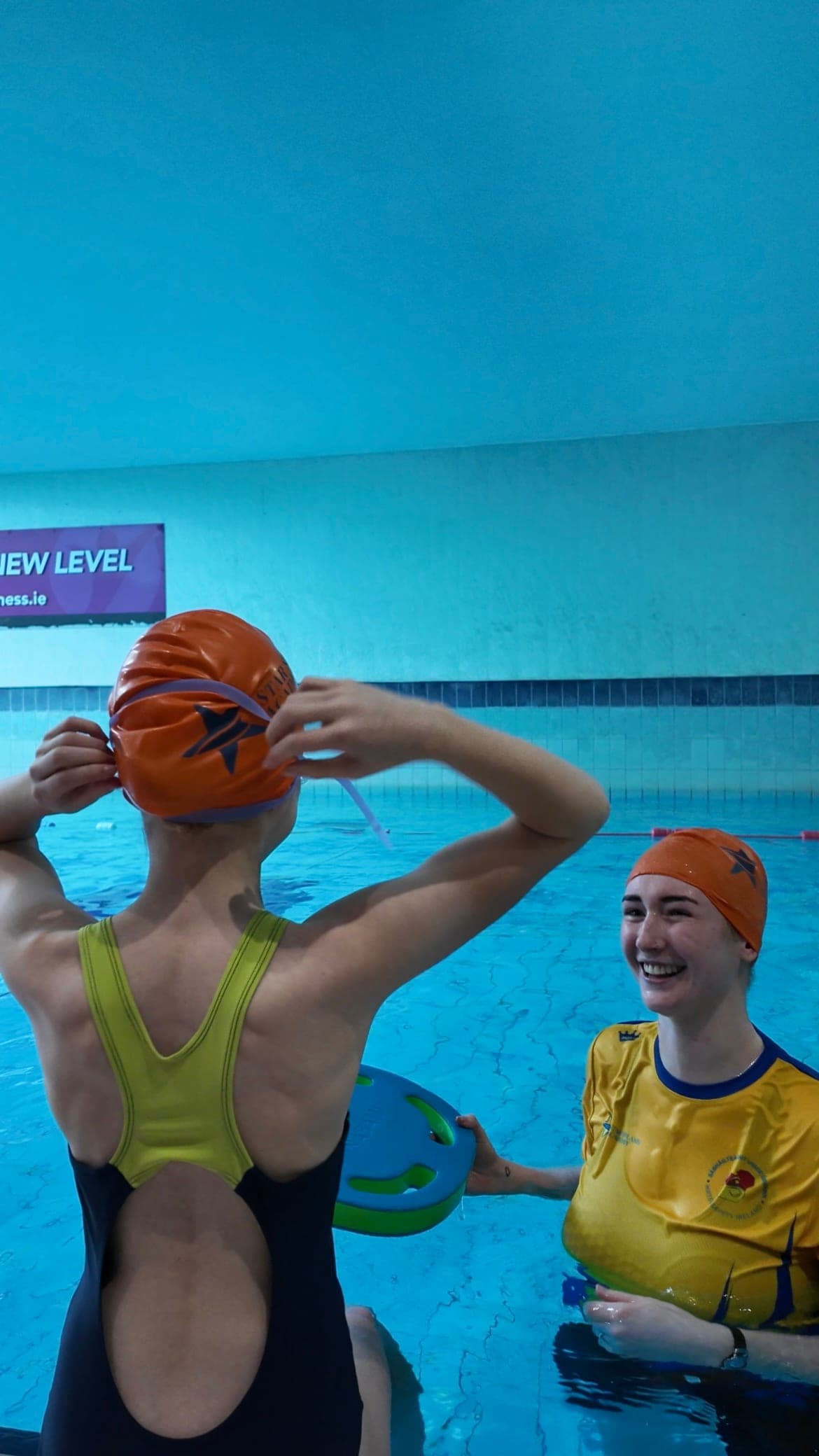 A swim teacher smiling as a swimmer adjusts their Star Splash Academy cap