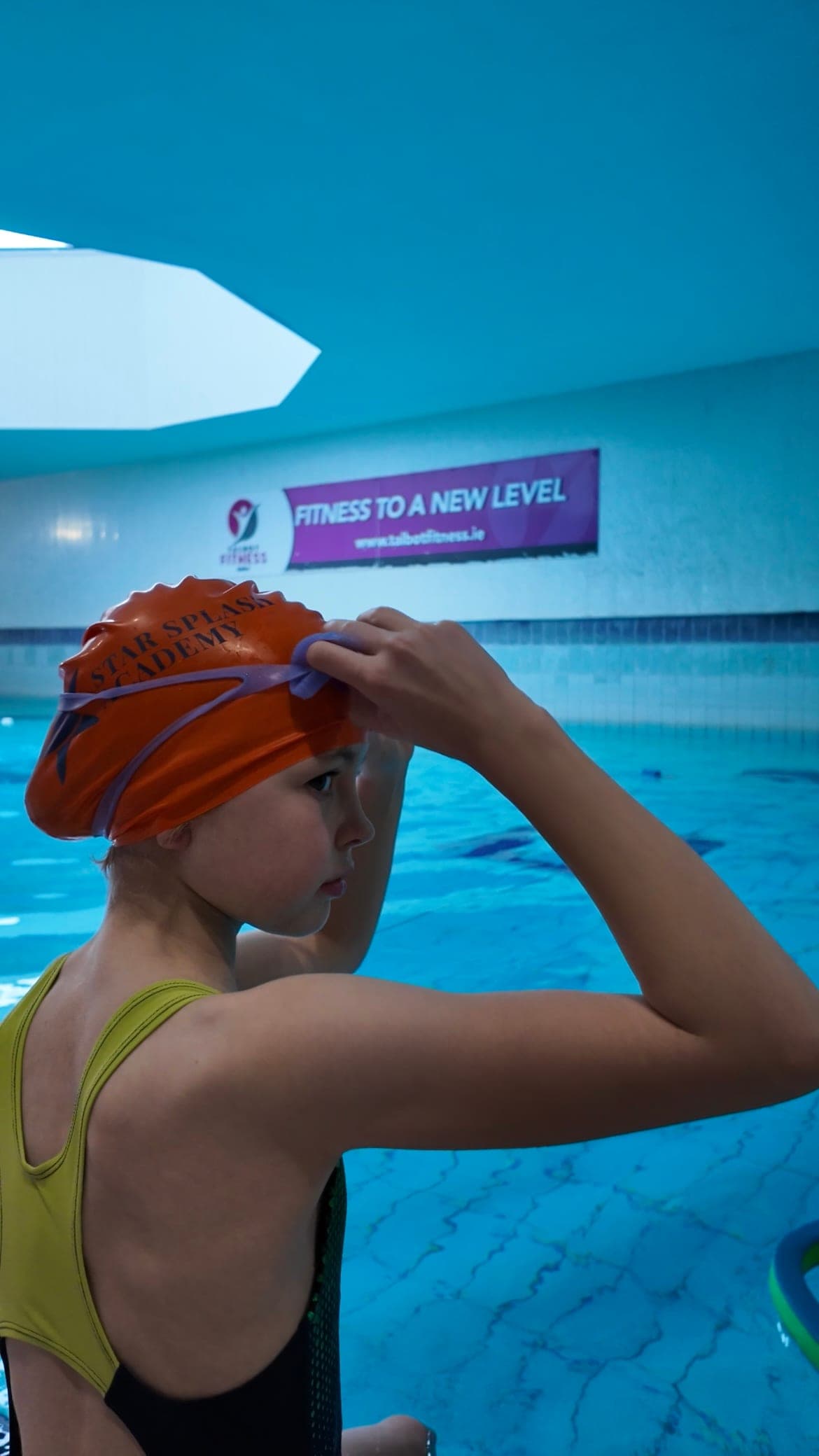 Close-up of a swimmer in an orange Star Splash Academy cap pulling on their goggles