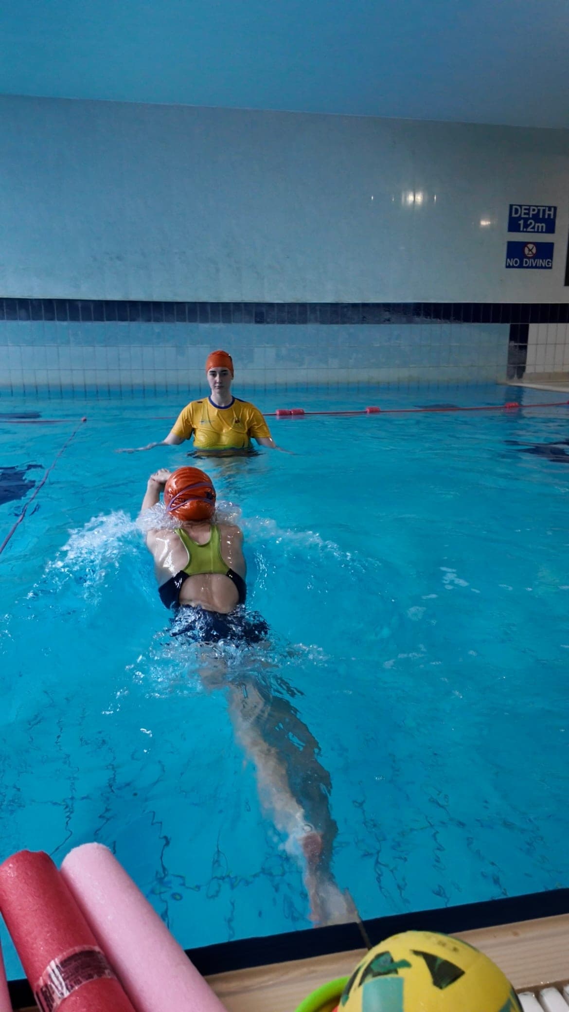 A swimmer practising front crawl as their teacher watches from the water