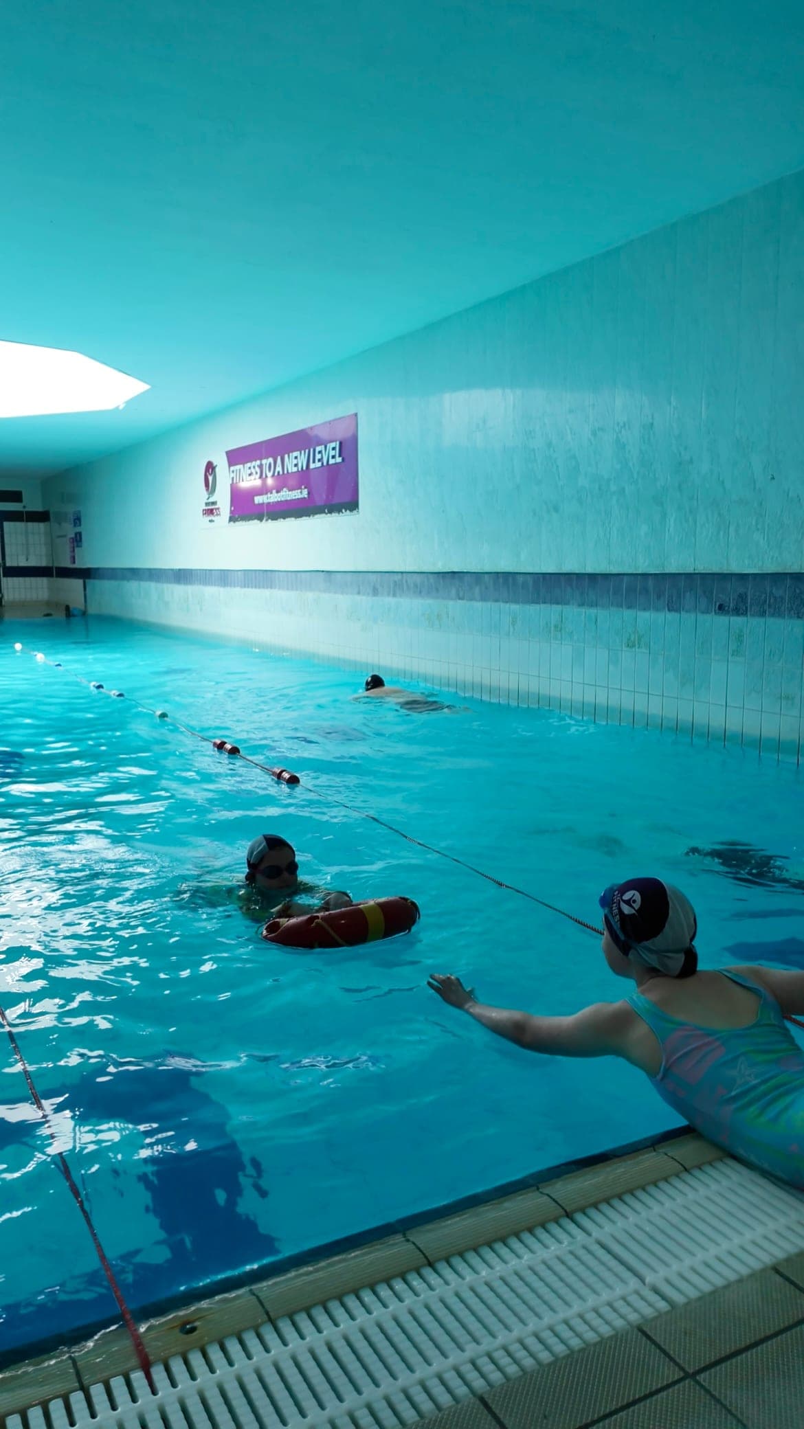 A swimmer performing a reach rescue with a ring buoy while an instructor supervises from the poolside